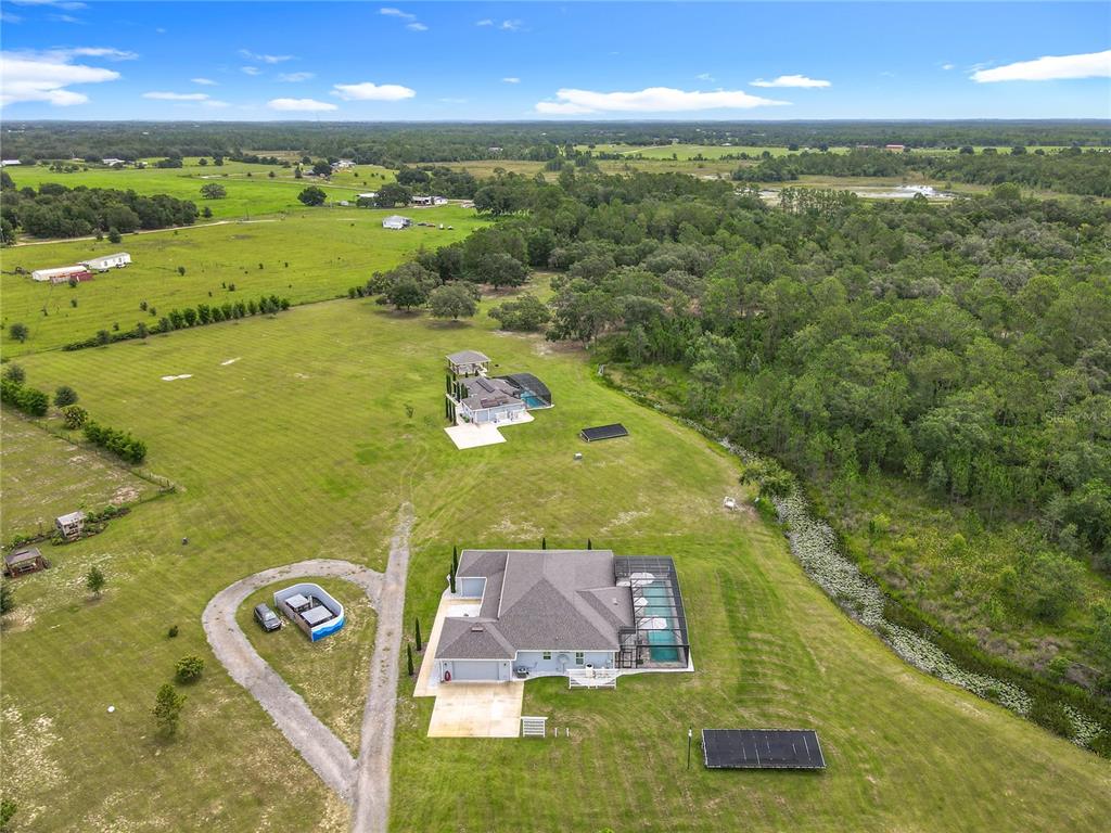 An aerial view shows two houses with swimming pools situated on a large, grassy lot — 10220 & 10224 BAY LAKE ROAD, GROVELAND, FL