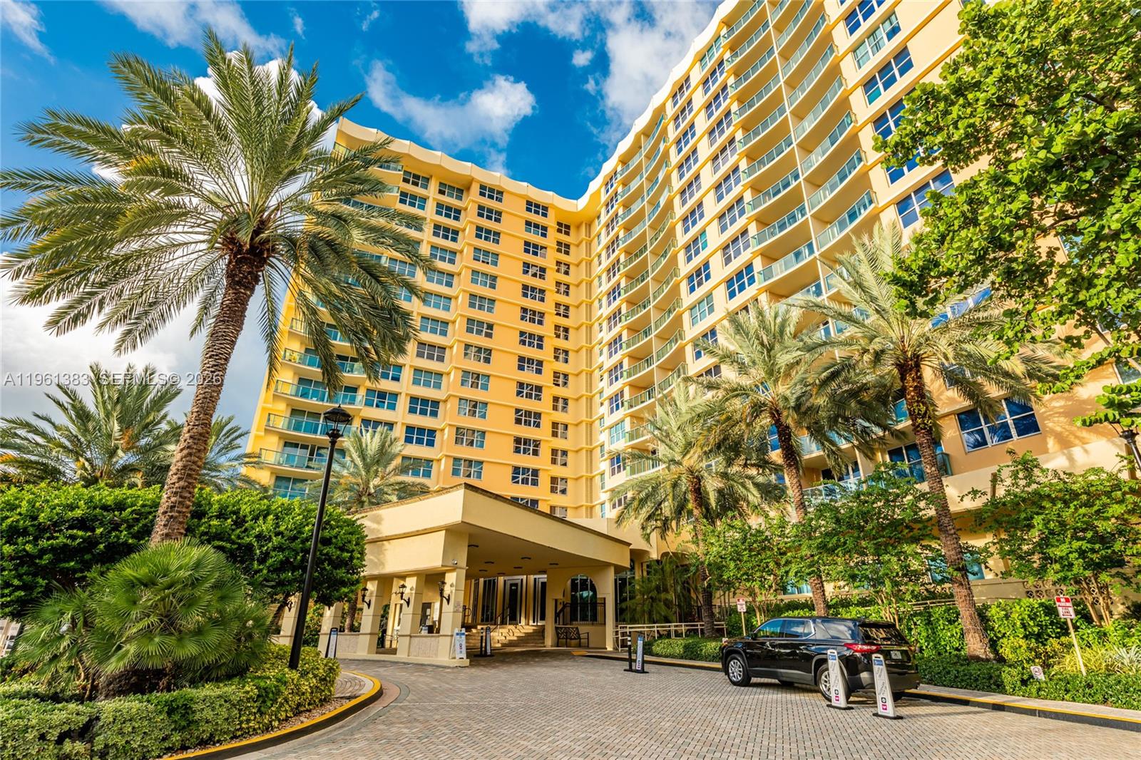 A multi-story yellow residential building features balconies, palm trees, and a paved driveway entrance — 2501 S Ocean Dr # 1617, Hollywood FL 33019, HOLLYWOOD, FL