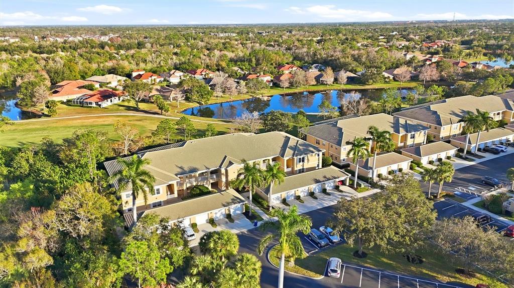 An aerial view shows multi-story apartment buildings with tan roofs near a pond and trees — 6342 GRAND OAK CIRCLE UNIT 204, BRADENTON, FL