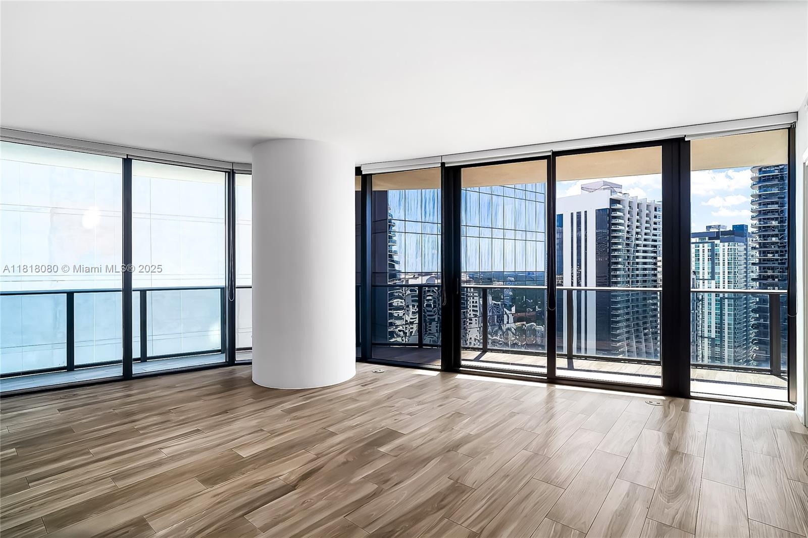 An empty room with wood-look tile floors, a central white column, and floor-to-ceiling windows — 801 S Miami Ave # 3704, Miami FL 33130, MIAMI, FL