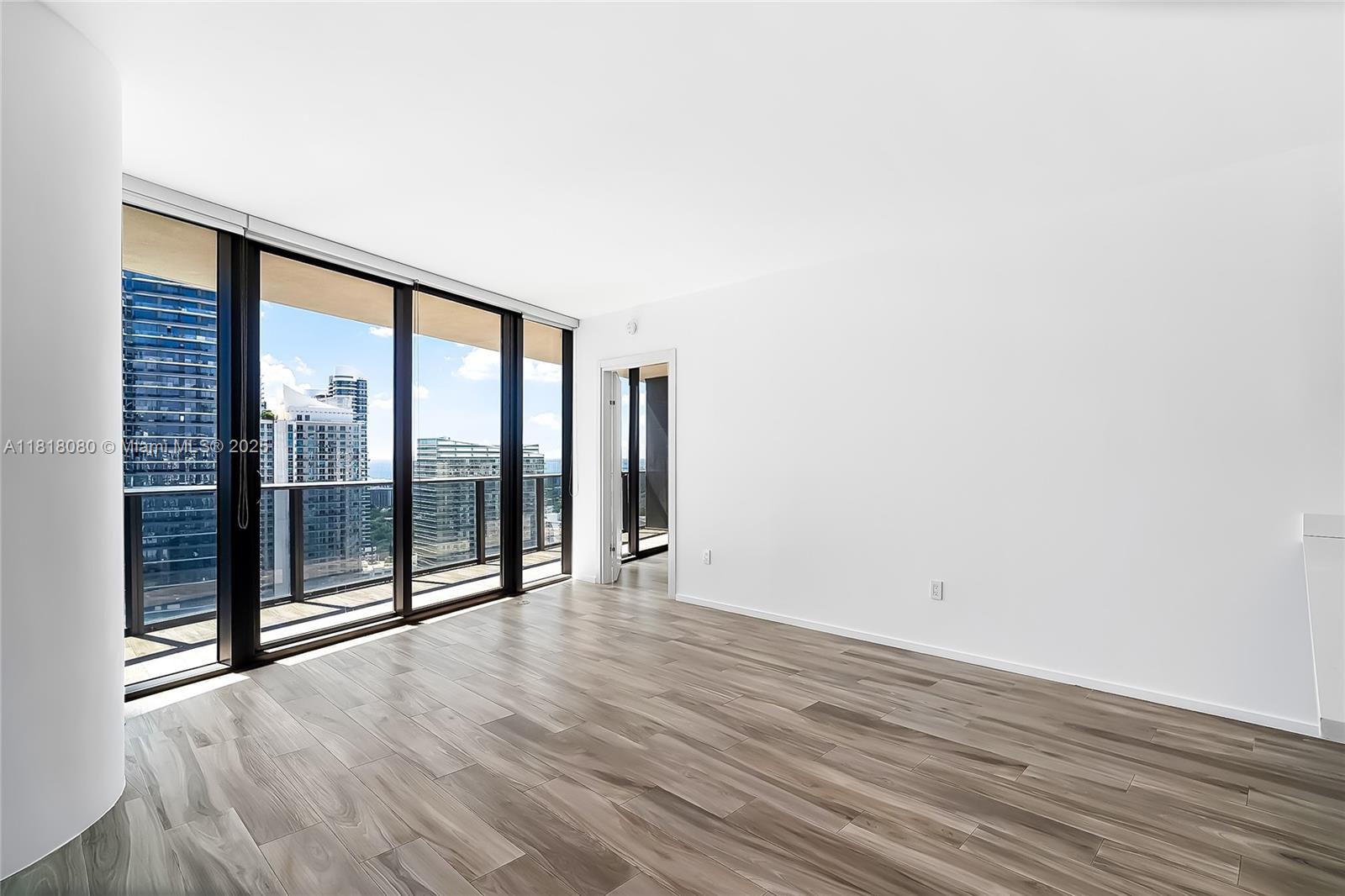 An empty room with wood-look tile flooring, white walls, and floor-to-ceiling windows overlooking city buildings — 801 S Miami Ave # 3704, Miami FL 33130, MIAMI, FL