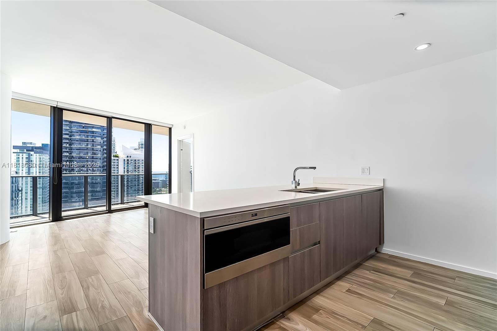 A modern kitchen island with a built-in microwave faces floor-to-ceiling windows overlooking a city skyline — 801 S Miami Ave # 3704, Miami FL 33130, MIAMI, FL