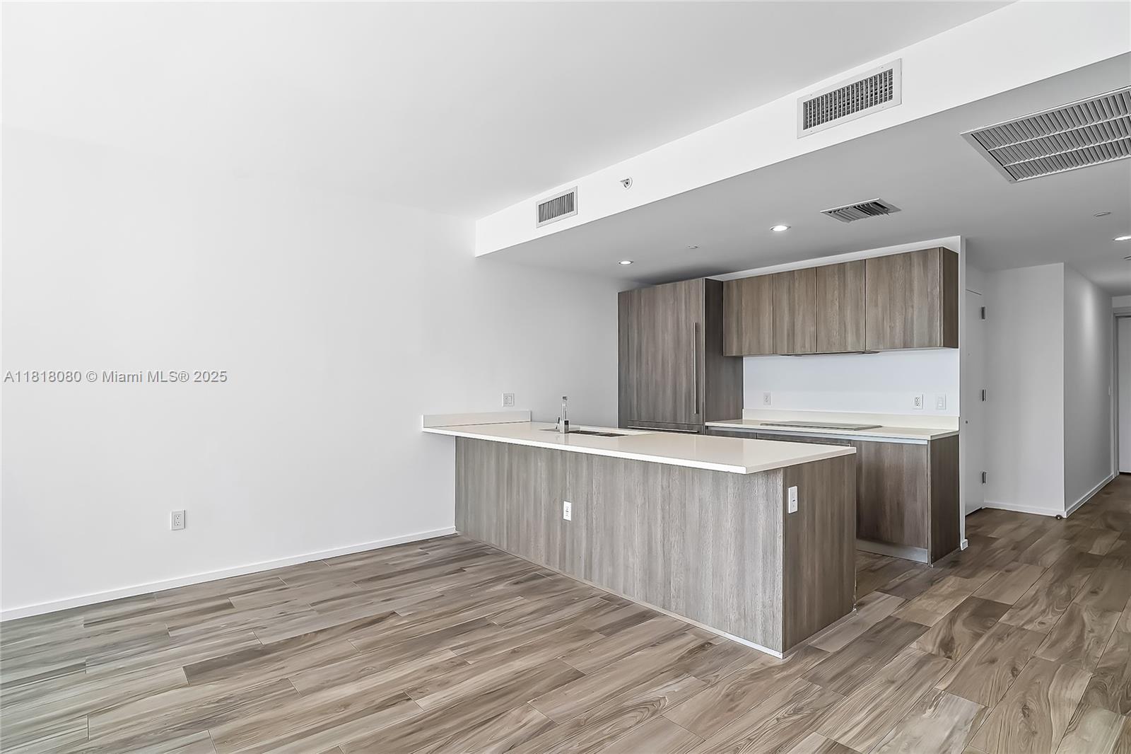 A modern kitchen features wood-toned cabinetry, a white countertop island, and light wood-look flooring — 801 S Miami Ave # 3704, Miami FL 33130, MIAMI, FL