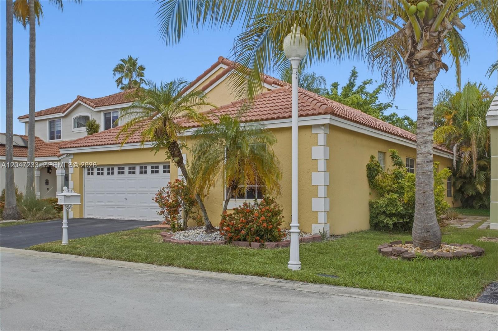 A yellow single-story house with a tile roof, a two-car garage, and palm trees — 411 Bermuda Springs Dr, Weston FL 33326, WESTON, FL