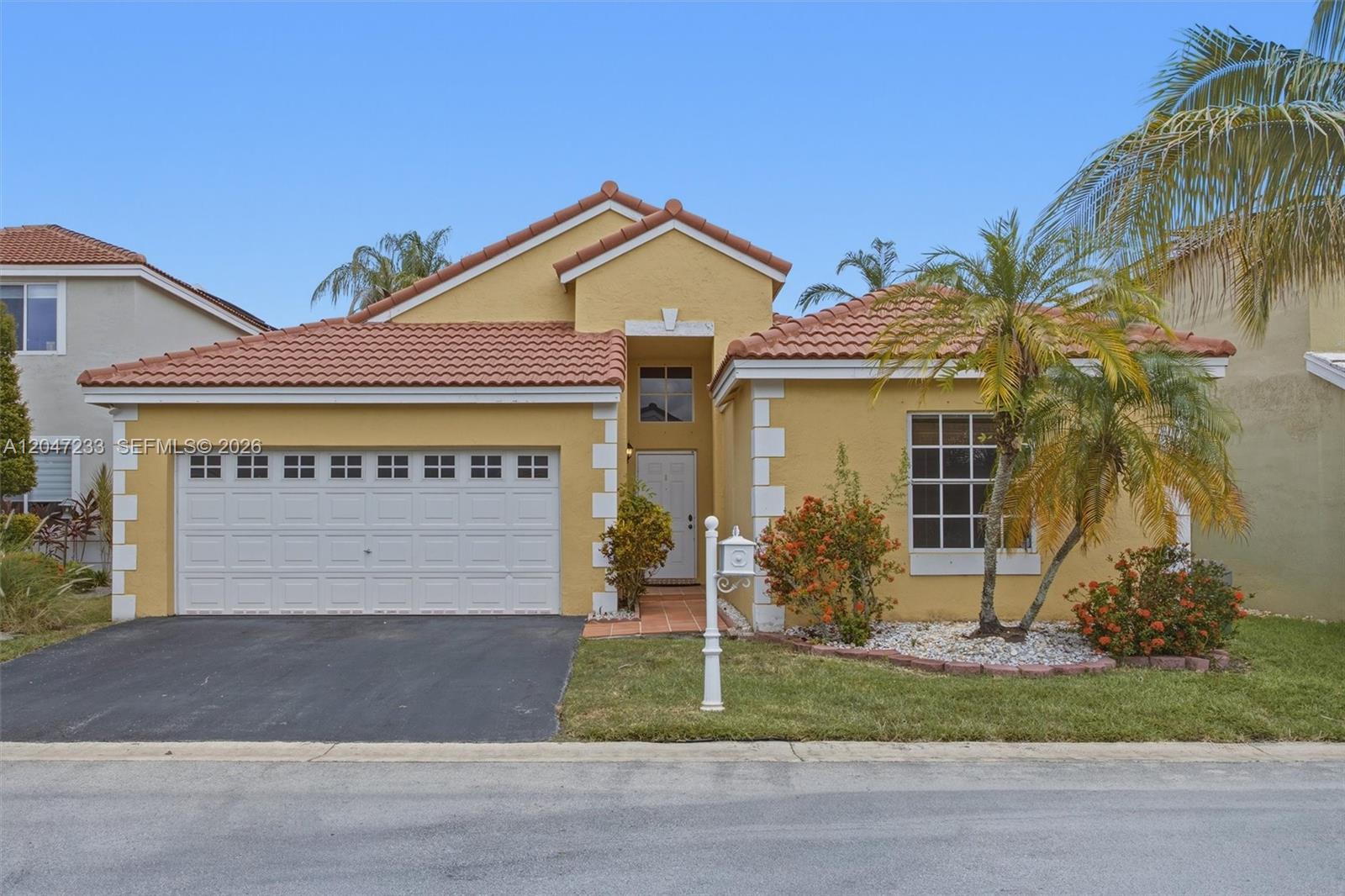 A yellow single-story house with a tile roof, a two-car garage, and a palm tree — 411 Bermuda Springs Dr, Weston FL 33326, WESTON, FL