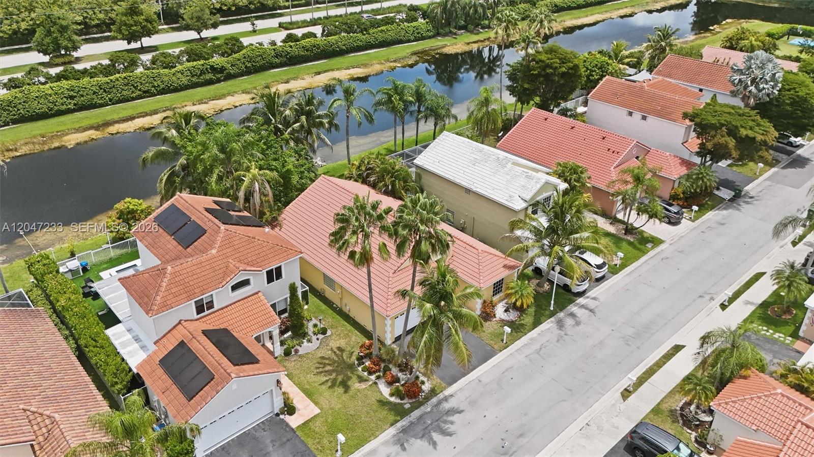 An aerial view shows several suburban houses with red tile roofs along a canal — 411 Bermuda Springs Dr, Weston FL 33326, WESTON, FL