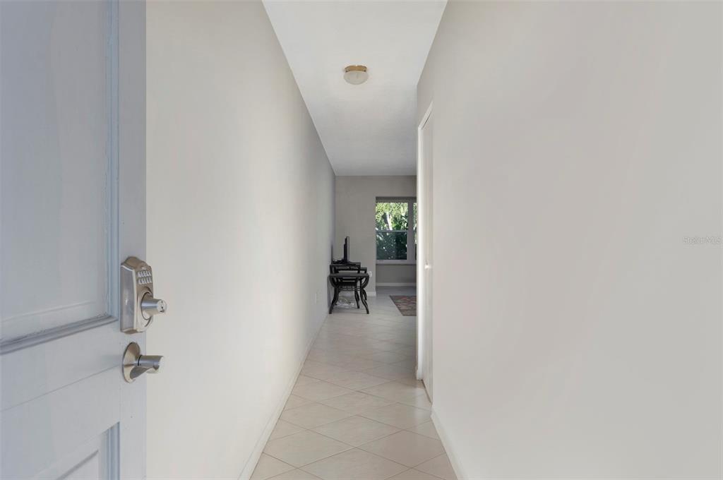 A narrow hallway with light-colored walls and tile flooring leads toward a windowed room — 5660 80TH STREET N UNIT A202, ST PETERSBURG, FL
