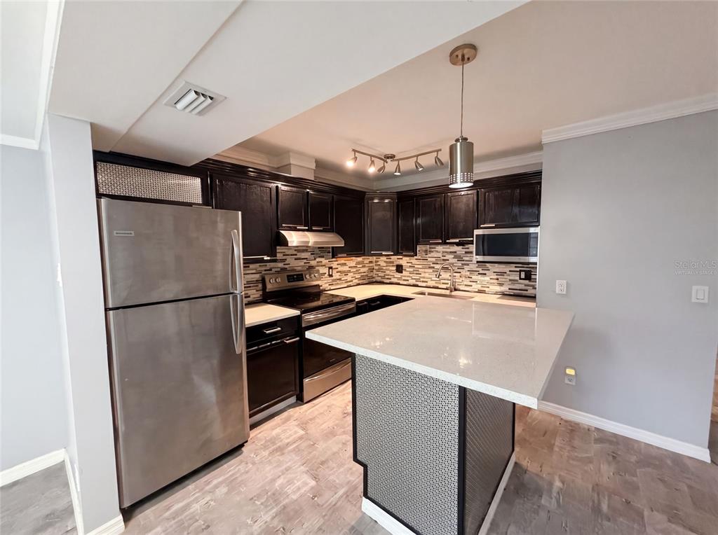 A kitchen features dark cabinetry, stainless steel appliances, a quartz island, and light wood flooring — 2308 S PARK AVENUE, SANFORD, FL