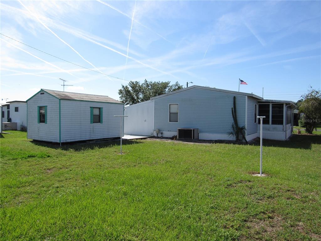 A light blue mobile home with an adjacent shed sits on a grassy lot — 37241 CORA AVENUE, ZEPHYRHILLS, FL