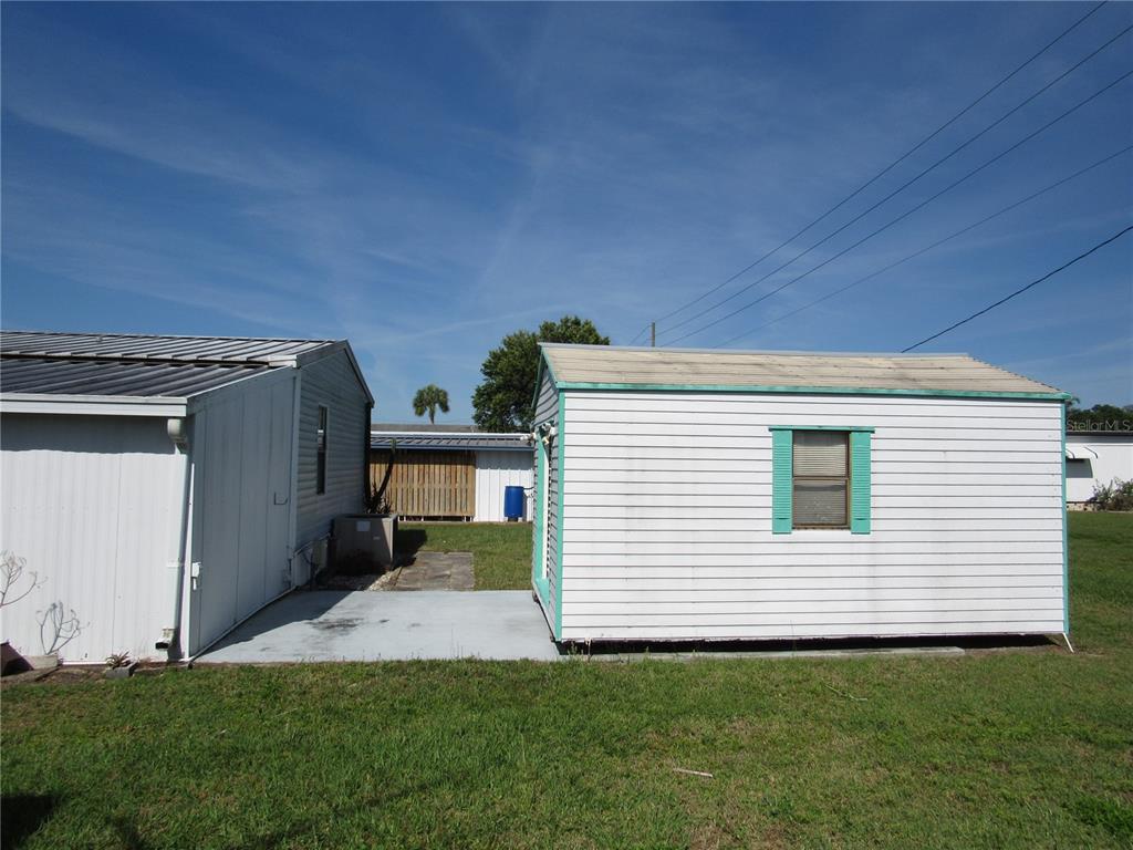 A white shed with a window sits on a lawn next to a larger building — 37241 CORA AVENUE, ZEPHYRHILLS, FL