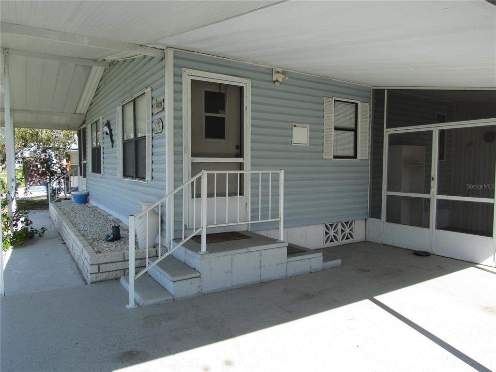 A light blue mobile home exterior features a covered carport, concrete steps, and a screened porch — 37241 CORA AVENUE, ZEPHYRHILLS, FL