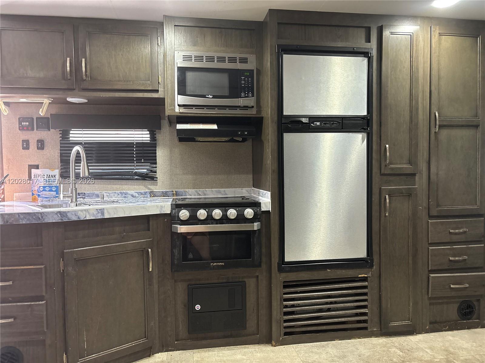 A kitchen in a recreational vehicle features dark wood cabinetry, stainless steel appliances, and countertops — 14165 NW 22nd Ct # A, Opa-Locka FL 33054, OPA-LOCKA, FL