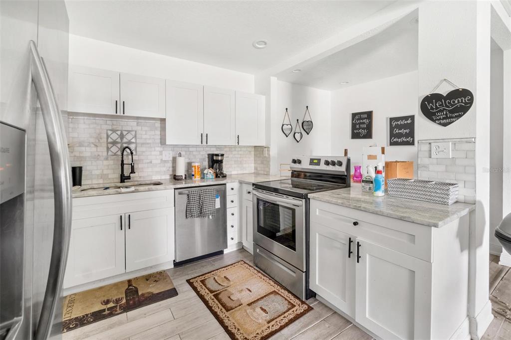 A kitchen with white cabinets, stainless steel appliances, and a light-colored tile backsplash — 6426 S HIMES AVENUE, TAMPA, FL