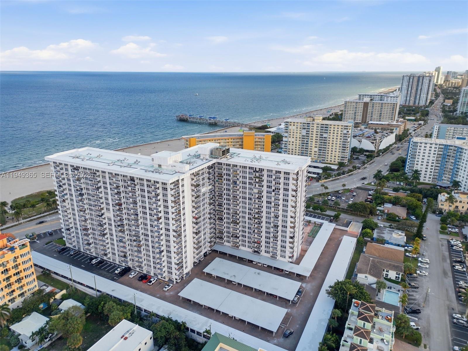 An aerial view shows a large white apartment complex with covered parking near the ocean — 405 N Ocean Blvd # 1528, Pompano Beach FL 33062, POMPANO BEACH, FL