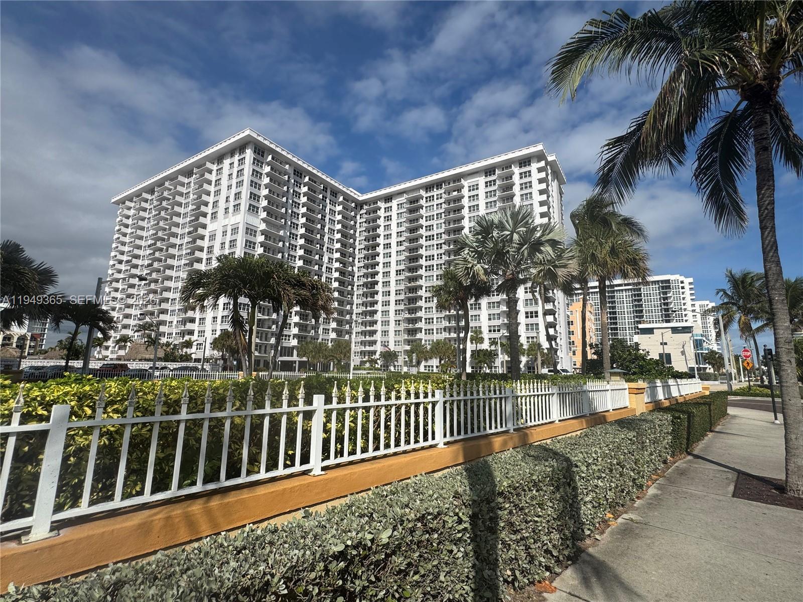 A white high-rise apartment building stands behind a white fence and manicured hedges — 405 N Ocean Blvd # 1528, Pompano Beach FL 33062, POMPANO BEACH, FL
