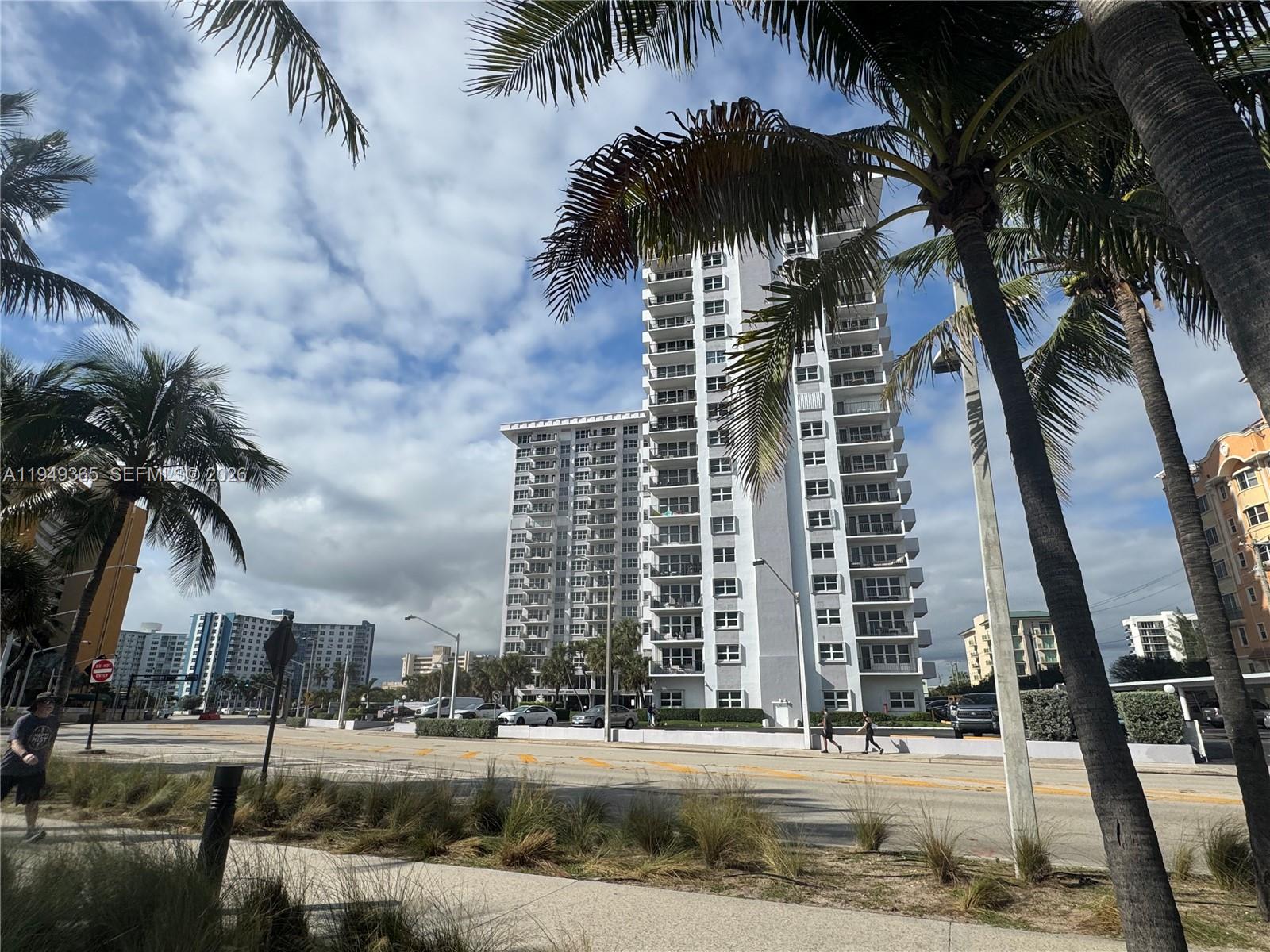 A tall white residential high-rise building stands behind palm trees along a paved road — 405 N Ocean Blvd # 1528, Pompano Beach FL 33062, POMPANO BEACH, FL