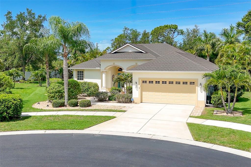 A single-story house with a beige exterior, a two-car garage, and palm trees in front — 122 CLEAR LAKE DRIVE, ENGLEWOOD, FL