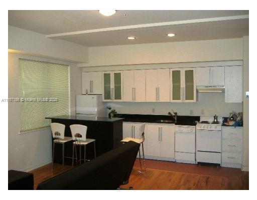 A kitchen with white cabinets, black countertops, a breakfast bar, and white appliances — 1521 Lenox Ave # 101, Miami Beach FL 33139, MIAMI BEACH, FL