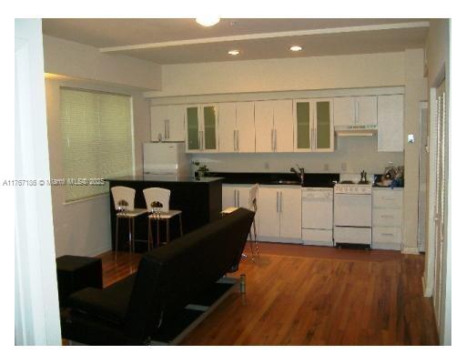 A kitchen with white cabinets and a black island opens into a living area — 1521 Lenox Ave # 101, Miami Beach FL 33139, MIAMI BEACH, FL