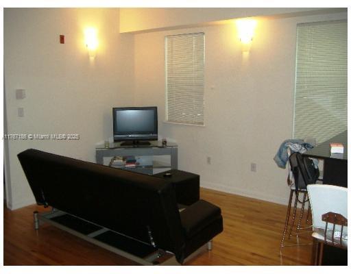 A living room with hardwood floors, a black futon, and a television on a stand — 1521 Lenox Ave # 101, Miami Beach FL 33139, MIAMI BEACH, FL