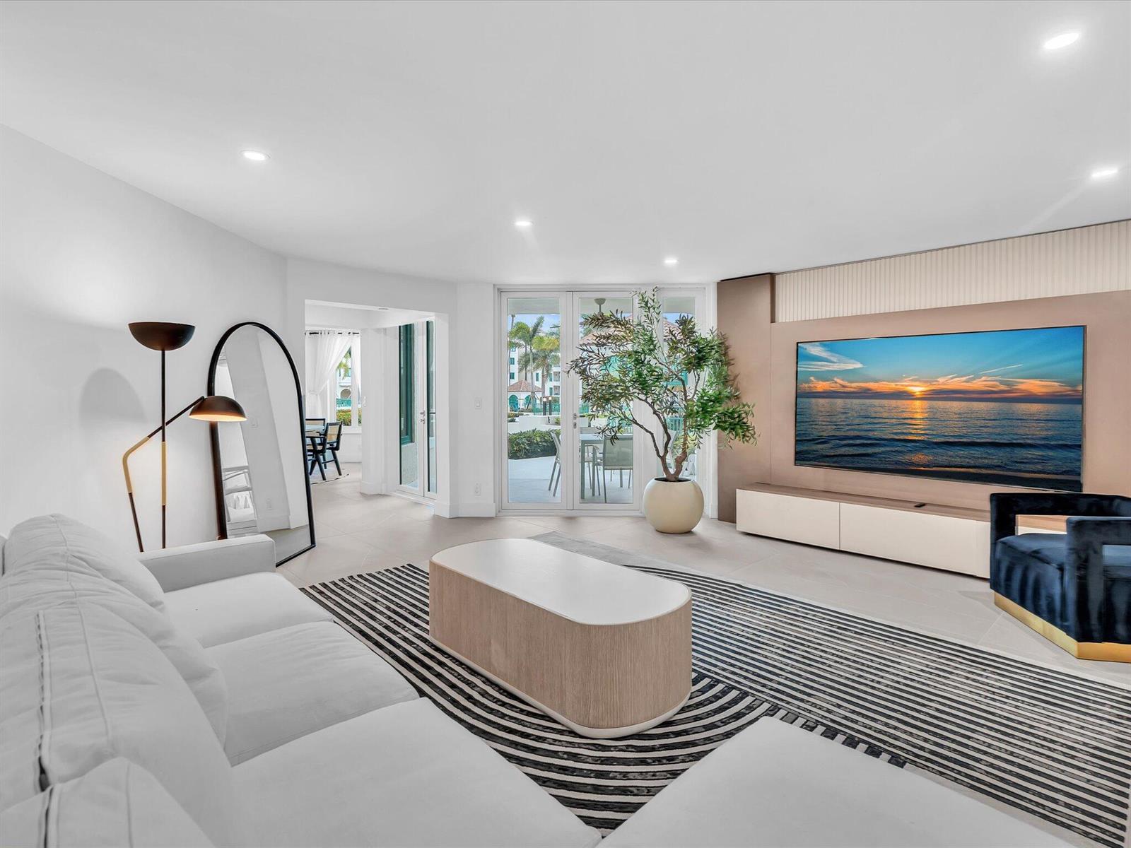 A modern living room features a white sectional, striped rug, and a large wall-mounted television — 120 SE 5th Avenue # 225, Boca Raton FL 33432, BOCA RATON, FL
