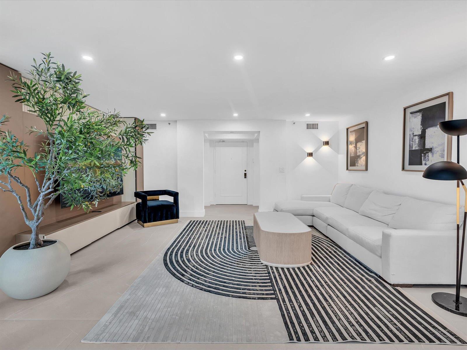 A modern living room features a white sectional sofa, a patterned rug, and a large plant — 120 SE 5th Avenue # 225, Boca Raton FL 33432, BOCA RATON, FL