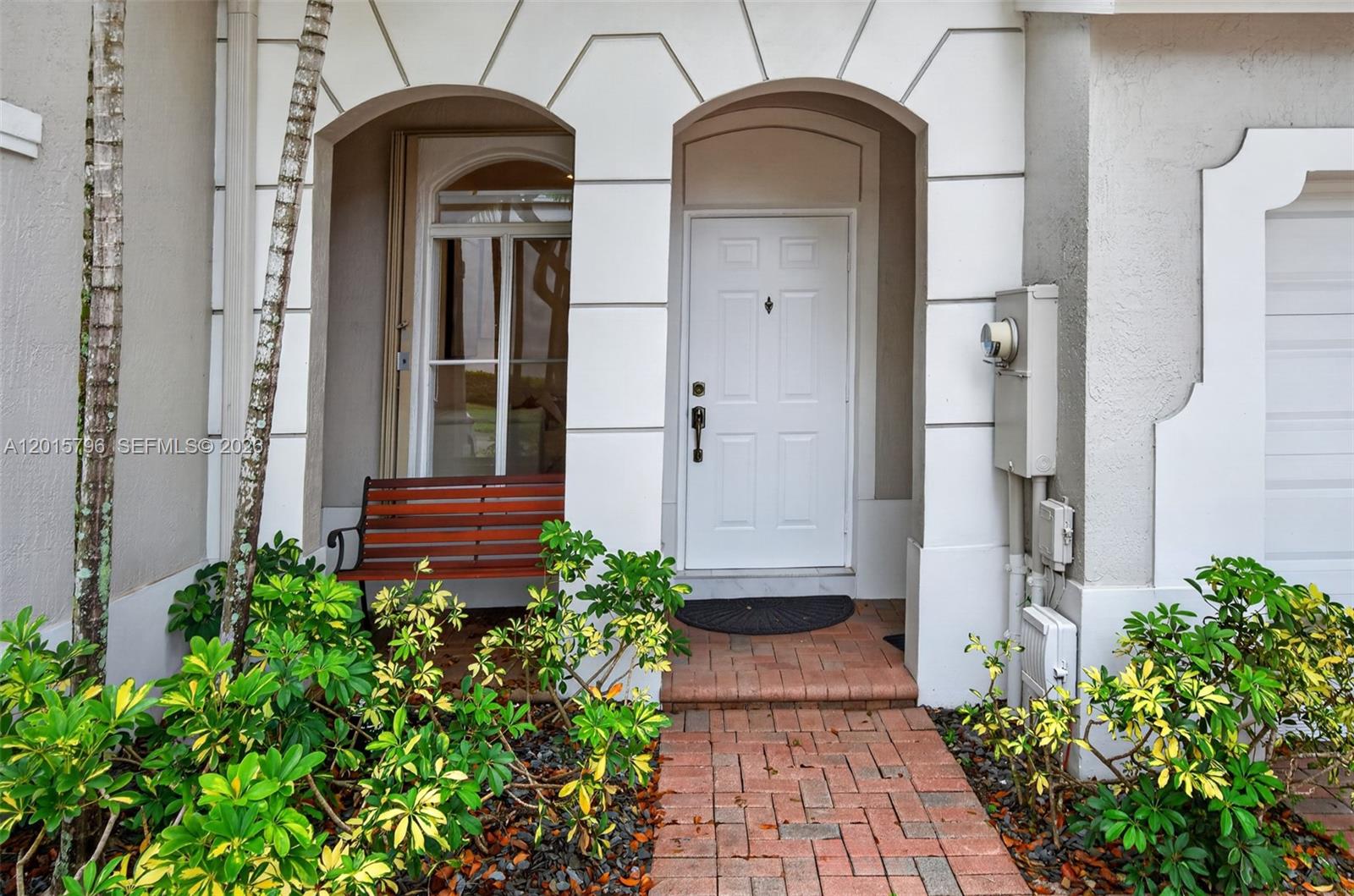 A white front door sits under an arched entryway next to a wooden bench — 11248 NW 56th St, Doral FL 33178, DORAL, FL