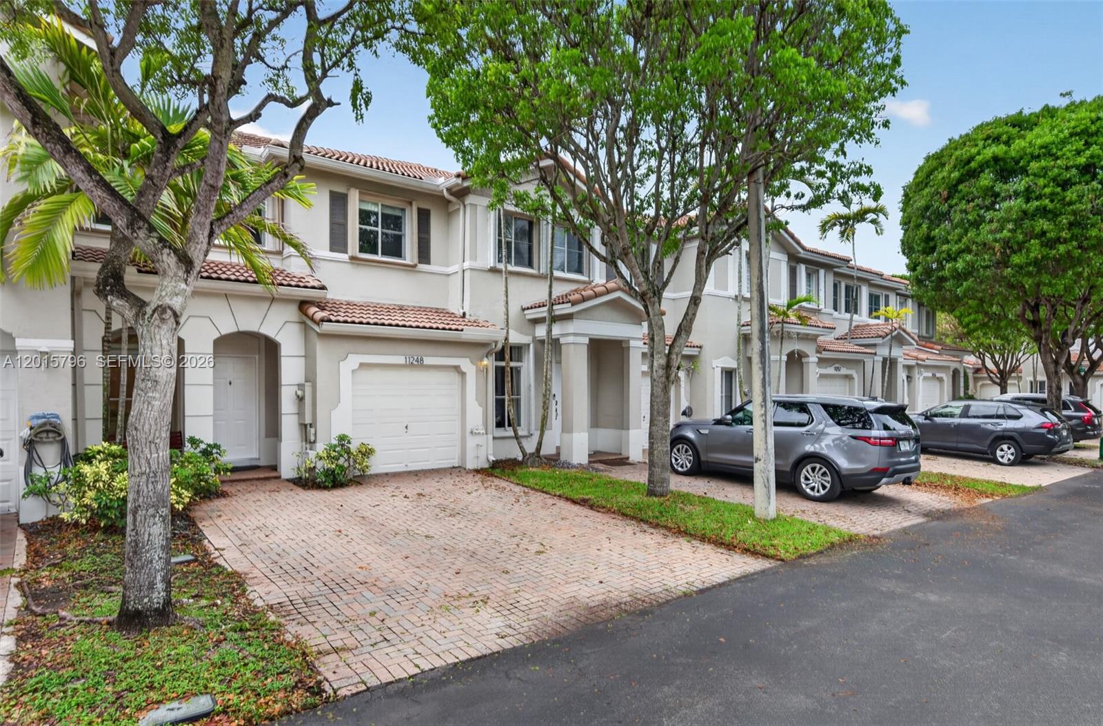 A row of two-story townhouses with brick driveways, garages, and mature trees in front — 11248 NW 56th St, Doral FL 33178, DORAL, FL