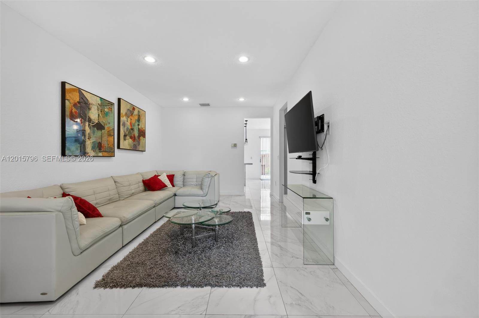 A living room features a white sectional sofa, glass coffee tables, and a wall-mounted television — 11248 NW 56th St, Doral FL 33178, DORAL, FL