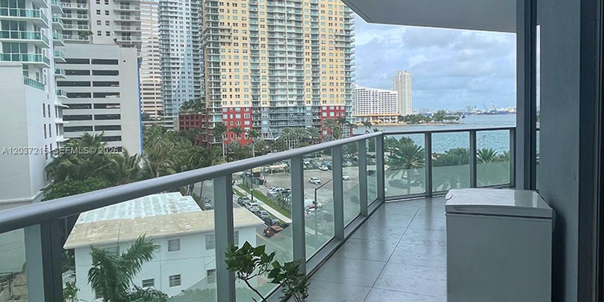 A balcony with glass railings overlooks a city street, nearby high-rise buildings, and the ocean — 1300 Brickell Bay Dr # 610, Miami FL 33131, MIAMI, FL