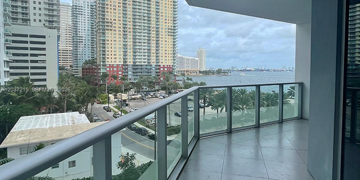 A balcony with a glass railing overlooks a city street, high-rise buildings, and the ocean — 1300 Brickell Bay Dr # 610, Miami FL 33131, MIAMI, FL