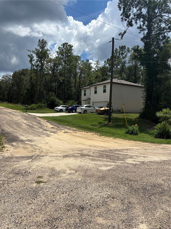 A two-story house with a driveway and three parked cars sits beside a dirt road — 875 E ELSTON PLACE, CITRUS SPRINGS, FL