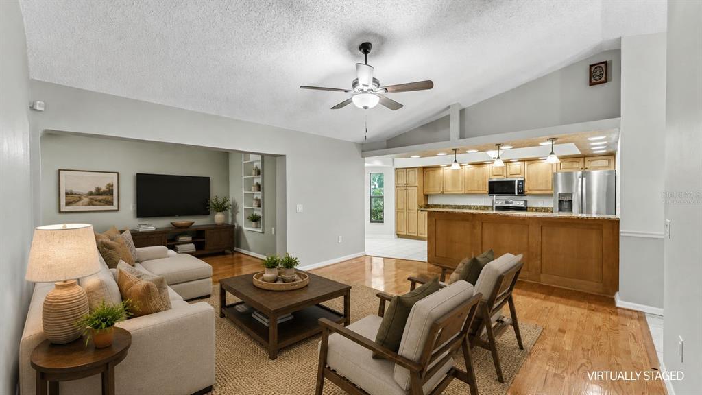 A living room with hardwood floors and a ceiling fan opens to a kitchen area — 6625 FORESTWOOD DRIVE W, LAKELAND, FL
