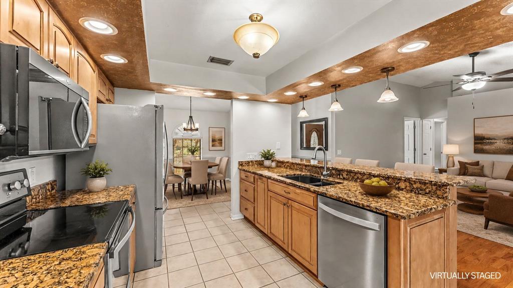 A kitchen with wood cabinets, granite countertops, and stainless steel appliances opens to a dining area — 6625 FORESTWOOD DRIVE W, LAKELAND, FL