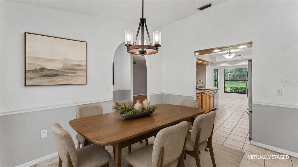 A dining room features a wooden table, upholstered chairs, a chandelier, and an arched doorway — 6625 FORESTWOOD DRIVE W, LAKELAND, FL