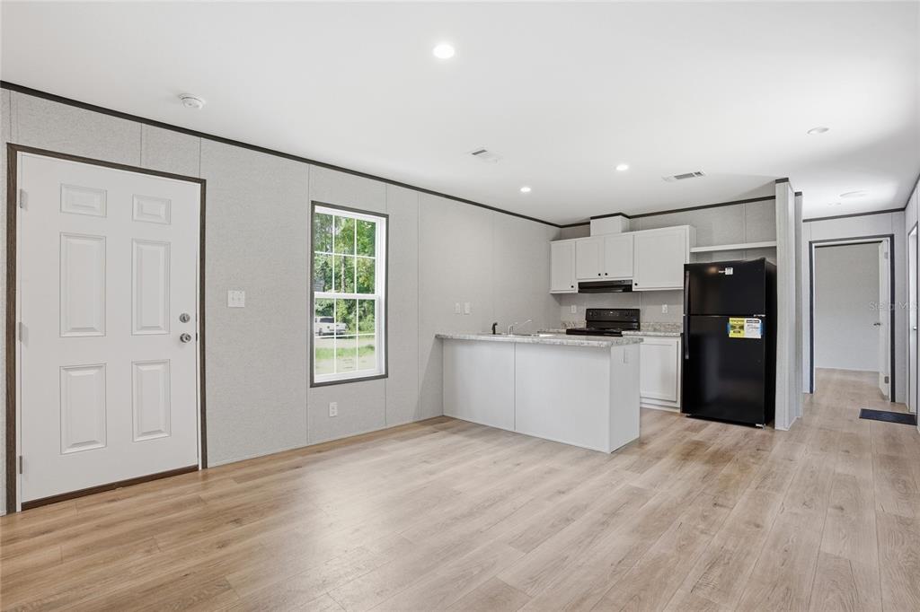 A kitchen with white cabinets, a black refrigerator, and an island opens to a living area — 11311 NW 13TH STREET, OCALA, FL
