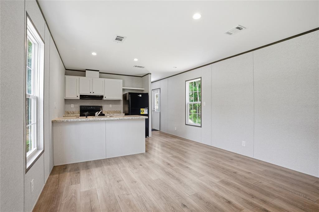 An open-concept kitchen and living area features light wood flooring, white cabinets, and white walls — 11311 NW 13TH STREET, OCALA, FL