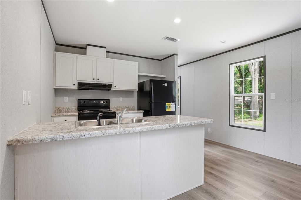 A kitchen features white cabinets, a black refrigerator, a black stove, and a granite-look island — 11311 NW 13TH STREET, OCALA, FL