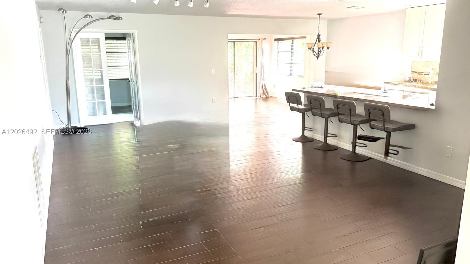 An open-concept living area features dark wood-look flooring, a kitchen island with barstools, and glass doors — 2736 Carnation Ct # 0, Delray Beach FL 33445, DELRAY BEACH, FL