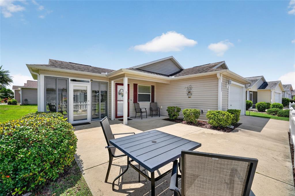 A patio with a table and chairs sits outside a house with beige siding — 1362 VIOLA COURT, THE VILLAGES, FL