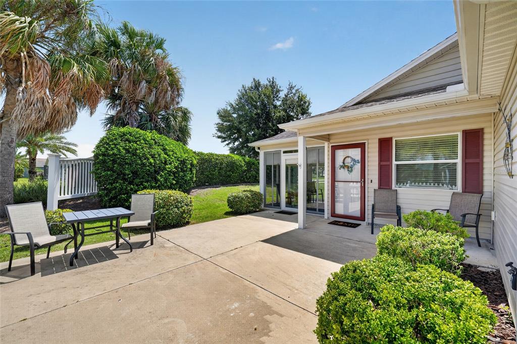 A concrete patio features outdoor furniture, a screened-in porch entrance, and manicured landscaping — 1362 VIOLA COURT, THE VILLAGES, FL