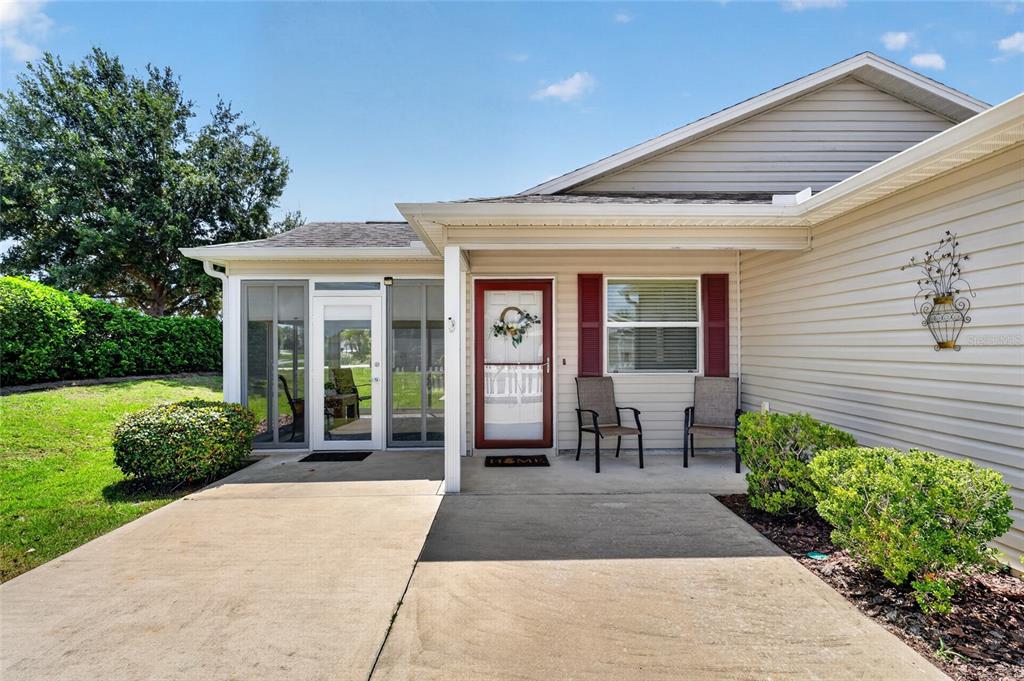 A beige house exterior features a concrete patio, a screened porch, and a front door — 1362 VIOLA COURT, THE VILLAGES, FL