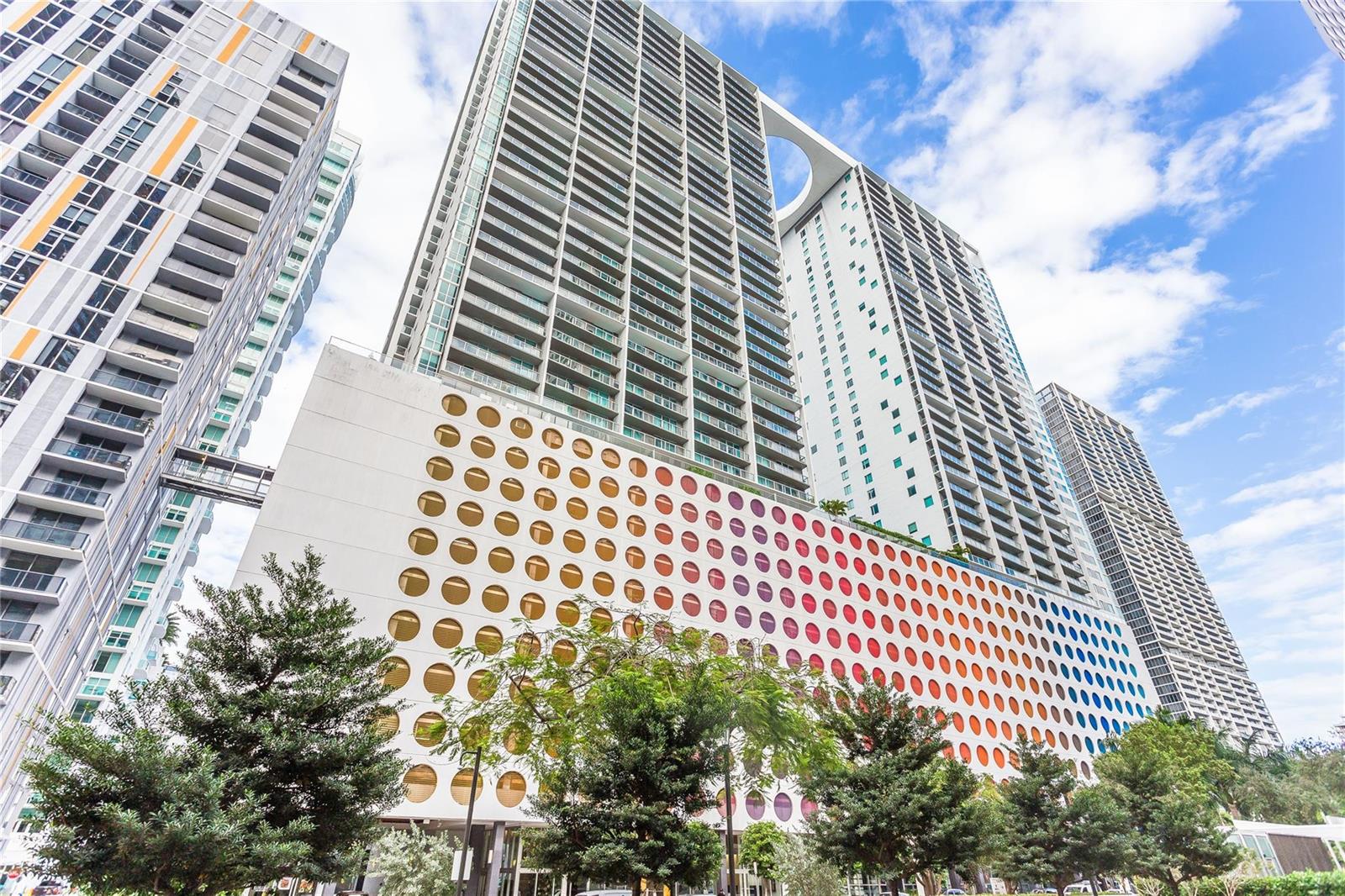 A low-angle exterior view of a modern high-rise building with a colorful circular-patterned parking garage — 55 SE 6th Street # 3500, Miami FL 33131, MIAMI, FL