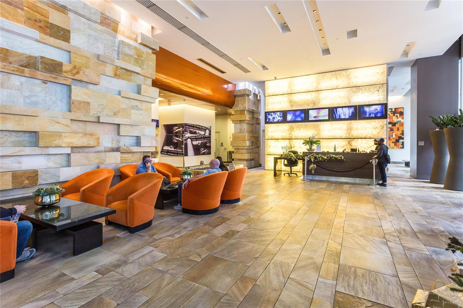 A modern hotel lobby features orange armchairs, stone walls, and a backlit reception desk — 55 SE 6th Street # 3500, Miami FL 33131, MIAMI, FL