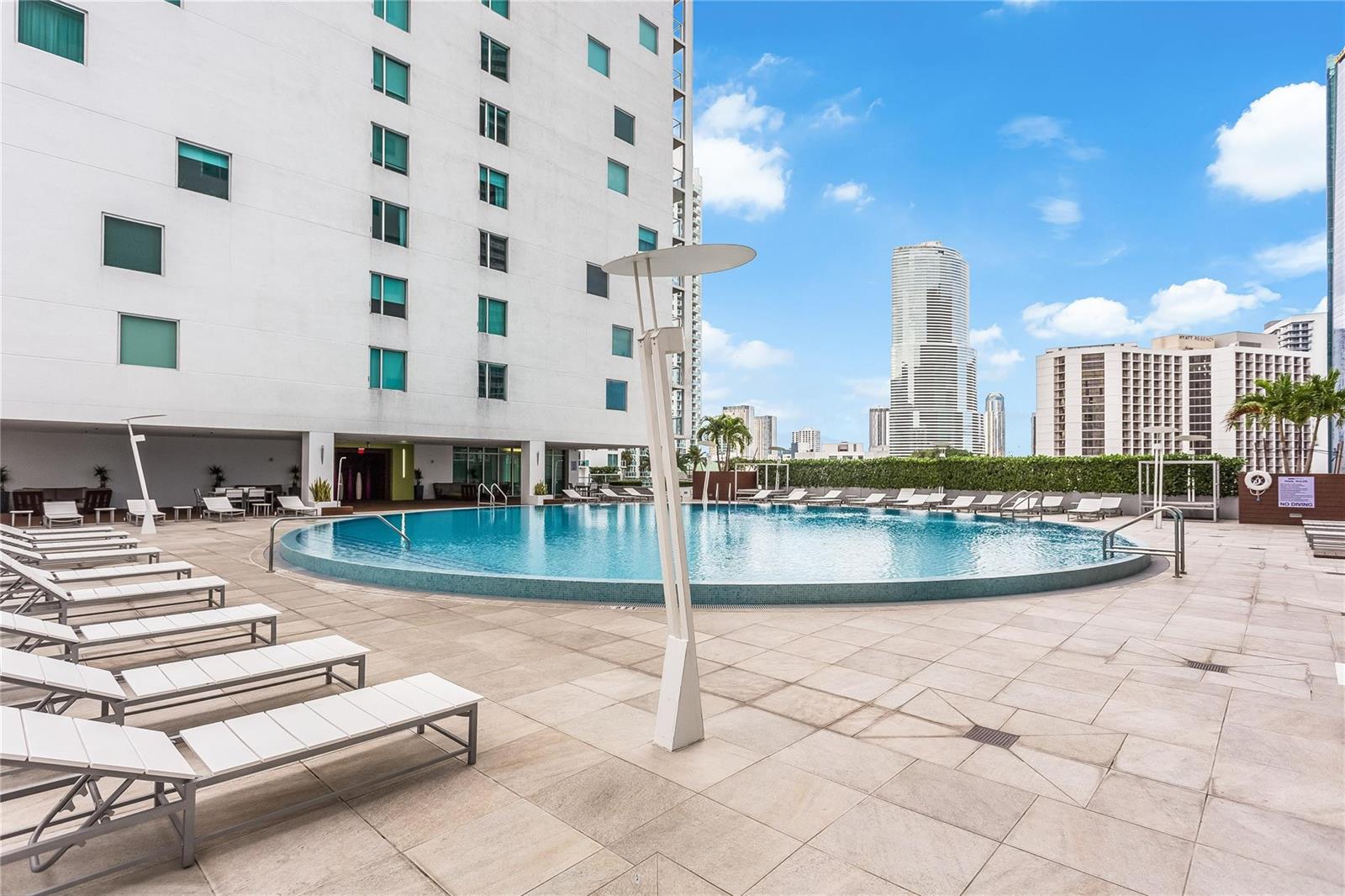 An outdoor swimming pool area with lounge chairs, a tall light fixture, and surrounding buildings — 55 SE 6th Street # 3500, Miami FL 33131, MIAMI, FL