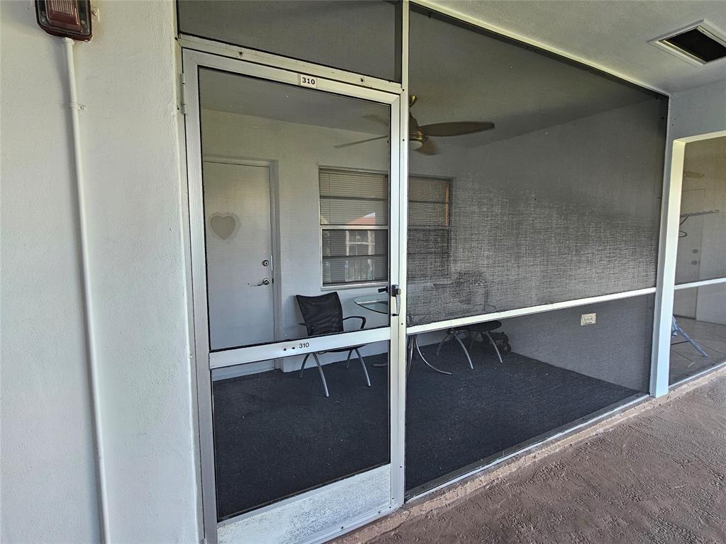 A screened-in porch features a glass door, a ceiling fan, and outdoor furniture — 580 Egret Drive # 310, Hallandale Beach FL 33009, HALLANDALE BEACH, FL
