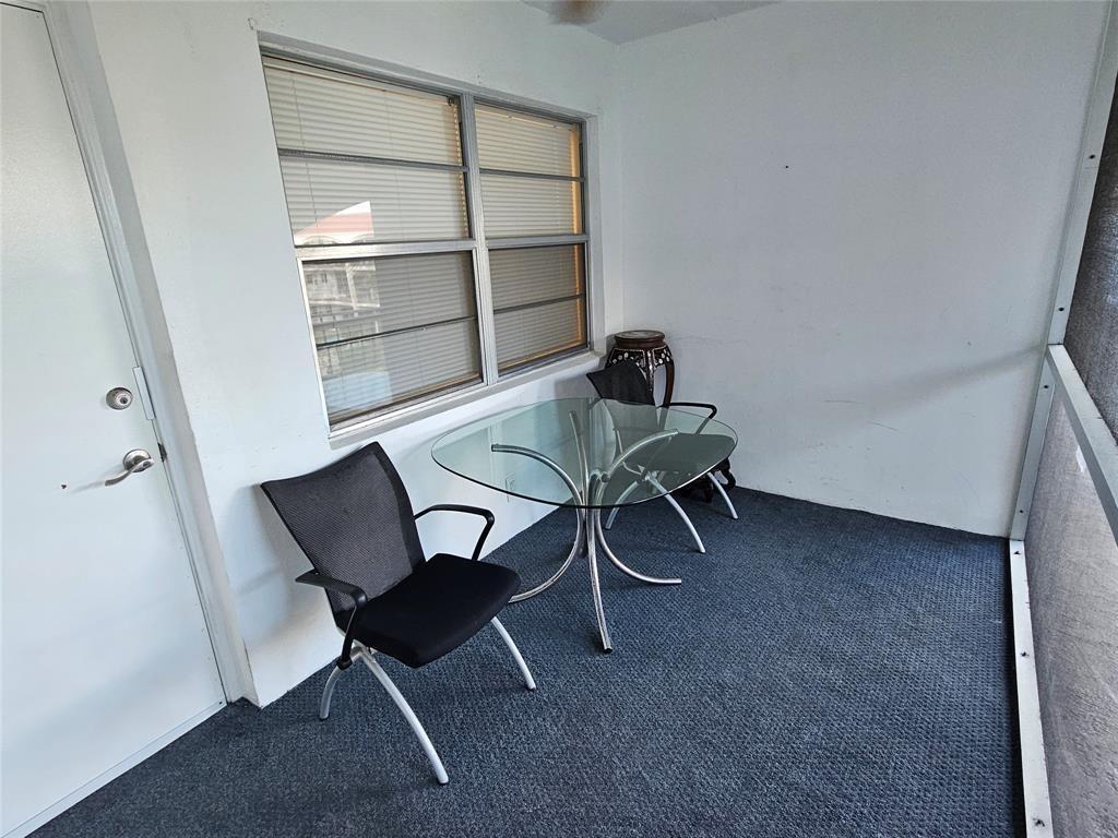 A glass-topped table and two chairs sit on the carpeted floor of a screened porch — 580 Egret Drive # 310, Hallandale Beach FL 33009, HALLANDALE BEACH, FL