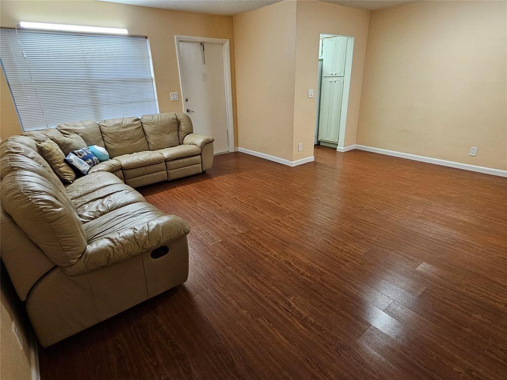 A living room features a large tan sectional sofa, wood-look flooring, and a white door — 580 Egret Drive # 310, Hallandale Beach FL 33009, HALLANDALE BEACH, FL