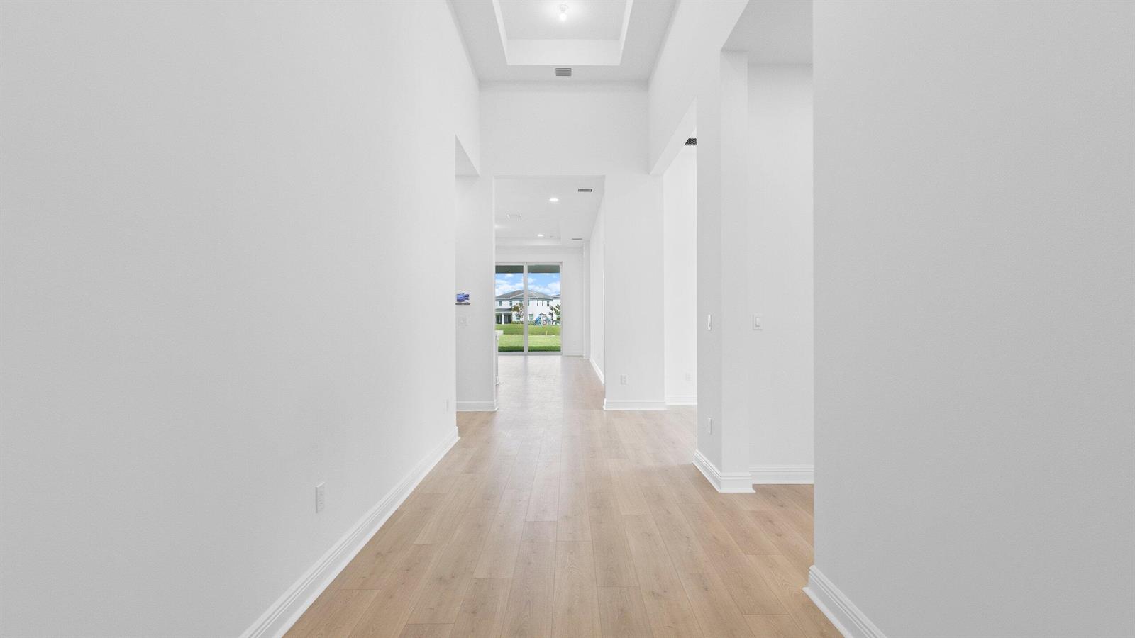 A bright, white hallway with light wood-look flooring leads toward a glass sliding door — 5468 Hutchinson Way, Westlake FL 33470, WESTLAKE, FL