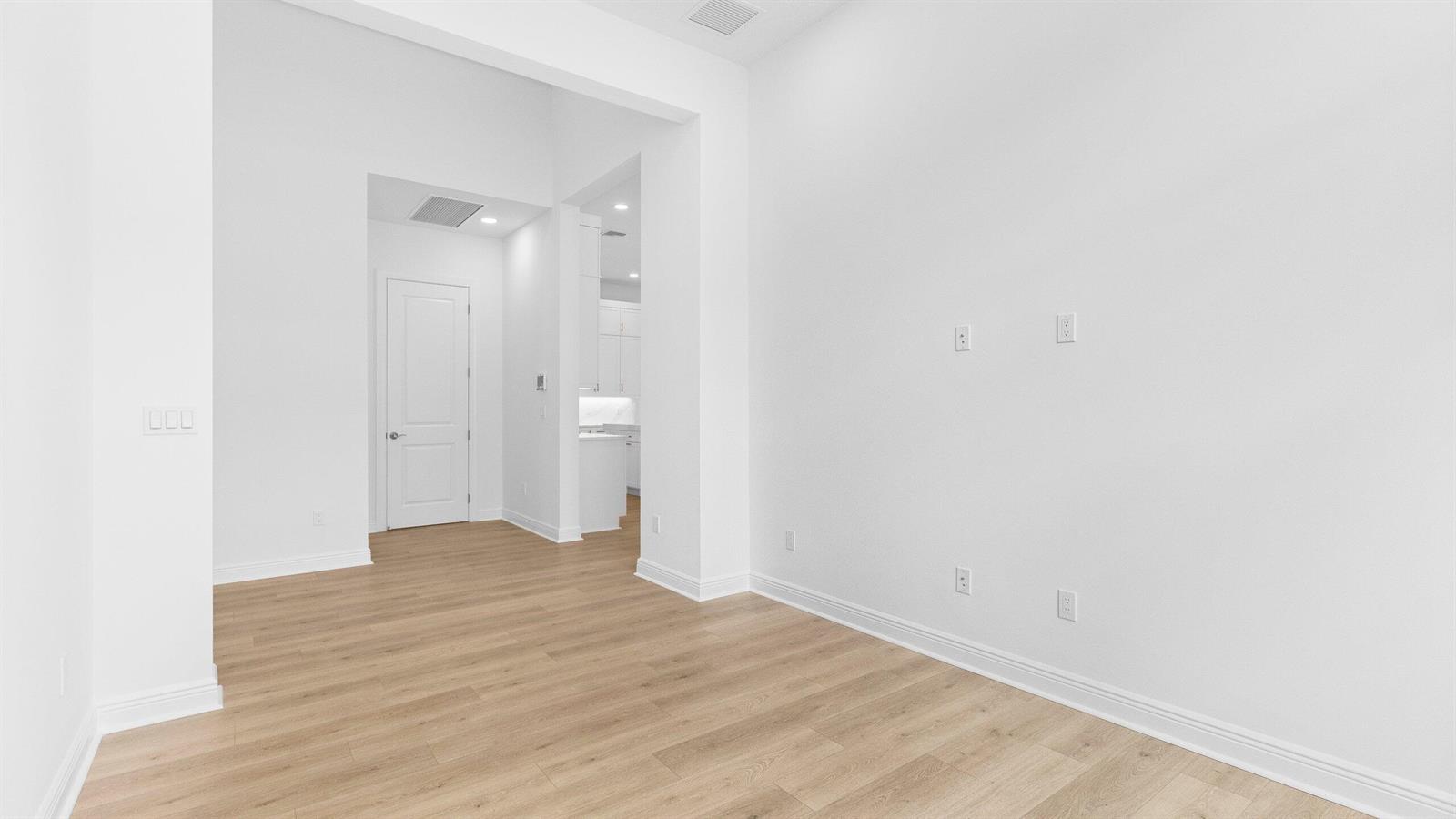 An empty room with light wood-look flooring, white walls, and a doorway leading to a kitchen — 5468 Hutchinson Way, Westlake FL 33470, WESTLAKE, FL